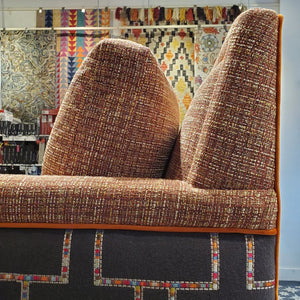 close up of custom sofa in stain-resistant nubbly textured fabric, contrast embroidered fabric on the arms and orange velvet piping