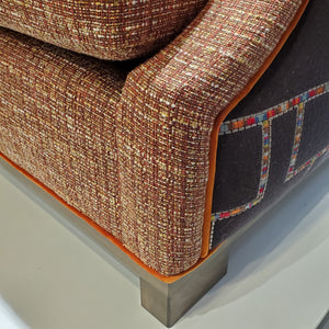 close up of custom sofa in stain-resistant nubbly textured fabric, contrast embroidered fabric on the arms and orange velvet piping