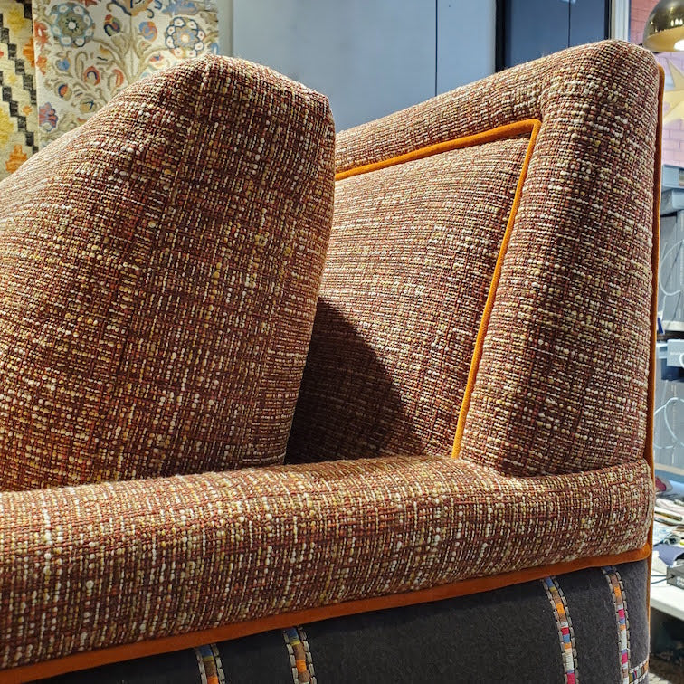 close up of custom sofa in stain-resistant nubbly textured fabric, contrast embroidered fabric on the arms and orange velvet piping